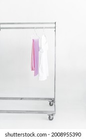 White Medical Doctor Or Physician Lab Coats With Pink Pants Hanging On Clothes Mobile Grey Hangers With Wheels, On White Background. Copy Space, Selected Focus. Vertical Picture.