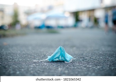 White Medical Mask Lies Like Trash On The Dirty Gray Asphalt In The City. Symbol Of Quarantine Fatigue And The Coronavirus Epidemic