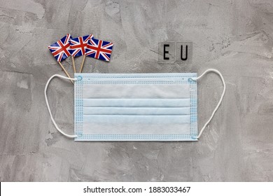 White Medical Mouth Mask, United Kingdom Flags And EU Sign On Gray Background. Coronavirus Covid-19 Mutation In UK, Lockdown, Brexit And Travel Concept. Flat Lay Copy Space