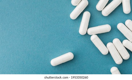White medical pills, tablets and capsules from pharmacy on turquoise background. Macro top down view with copy space. 