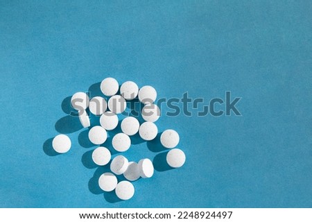 White medical pills and tablets on a blue background with space for copy. Top view. Vitamin tablets scattered on the table. Round white pills of vitamins.