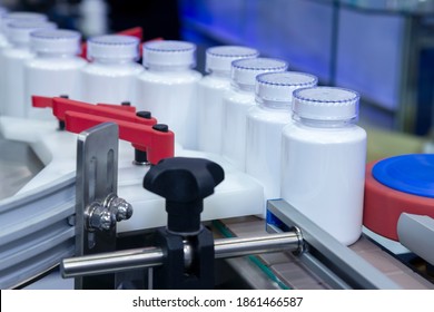 white medicine plastic bottle on production line of conveyor at filling machine in medical factory. selective focus. pharmaceutical manufacturing and industry concept.