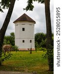 White medieval defensive tower in the park with trees in the background and cloudy sky, Bykhov city, Mogilev region, Belarus