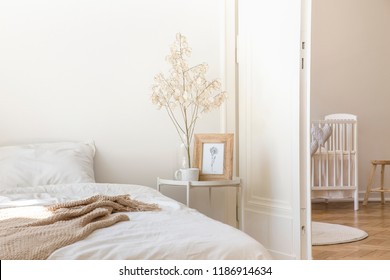 White Metal Bedside Table With Coffee Mug, Twig In Glass Vase And Simple Poster In Frame Placed By The Bed In Real Photo Of White Bedroom Interior