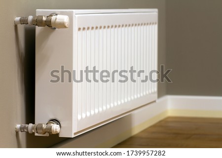White metal heating radiator mounted on gray wall inside a room.