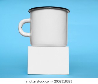 A white metal mug and a white box on a blue background. Mock up. 