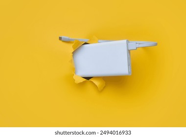 A white metal power bank protrudes from a torn hole in yellow paper. Concept of smartphone charging and mobile energy independence. - Powered by Shutterstock