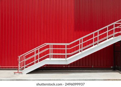 A white metal staircase is leaning against a red wall. The staircase is empty and the wall is painted in a bright red color. Scene is calm and peaceful, as the staircase is not in use - Powered by Shutterstock