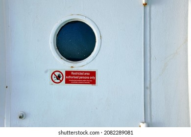 White metal weather tight exit door from superstructure of cargo merchant container vessel with copy space and red safety warning sign prohibiting enter non authorised person inside the ship.
