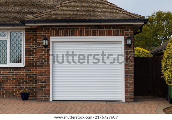 White metallic garage door in the\
side of a suburban bungalow with lanterns either\
side