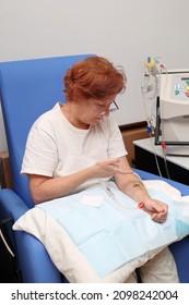 White Middle Age Woman Patient With Kidney Failure Preparing For Home Hematological Dialysis, Inserting A Needle In Her Arm