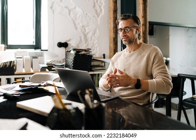 White middle-aged man in eyeglasses heaving meeting on a laptop computer in modern office - Shutterstock ID 2232184049