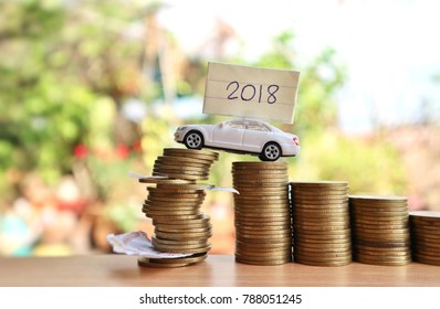 White Miniature Car With “2018” Year On Paper Drives On Rolls Ladder Of Gold Coins To Unstable Roll Of Money With Pieces Of Lottery On Wood Table In Blur Natural Tree Bright Light