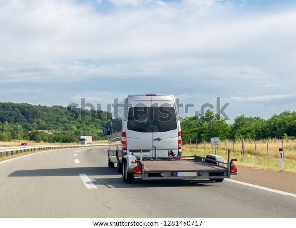 White minibus with empty tow truck transporter on\
highway. Space for text