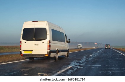 A White Minibus Transports People To Another City On A Wet Highway. The Concept Of Passenger Transportation On Minibuses, International, Copy Space