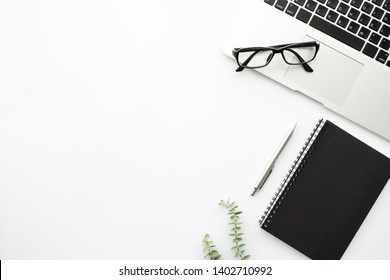 White Minimalist Office Desk Table With Laptop Computer, Notebook With Pen And Eye Glasses. Top View With Copy Space, Flat Lay Minimal Style.