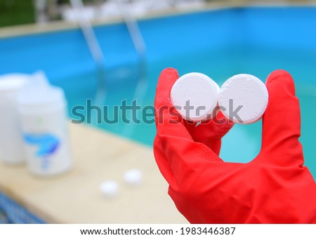 White mini-tablet of chlorine in the hand of the staff for disinfection of swimming pools. The beginning of the swimming season is hot summer. Rubber protective red glove. Water purification.