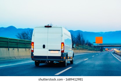 White Minivan At Road. Mini Van Auto Vehicle On Driveway. European Van Transport Logistics Transportation. Auto With Driver On Highway.