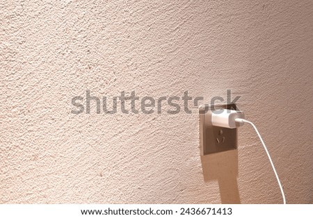 white mobile phone charger stabbing in plug in socket on room wall 