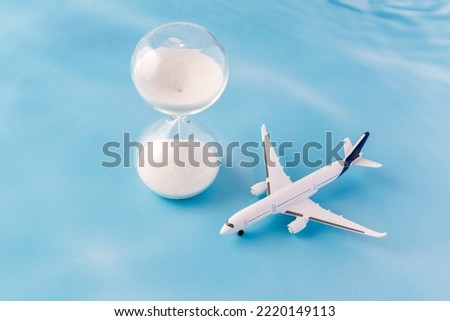 White model airplane and hourglass on blue background with copy space.  Last minute travel concept.