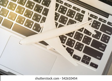White model airplane lands on a laptop keyboard. An idea of global things concerns aviation can be done online at hand ie. ticket booking, flight schedule tracking, shipping