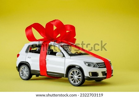 White model car with bow on a yellow background. Car as gift, surprise.