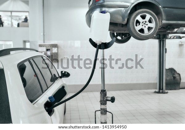 White modern auto after planned diagnosis and\
overhaul are refueling with gasoline from white canister  in\
service station before happy owner will take it away. Auto service\
and technician concept