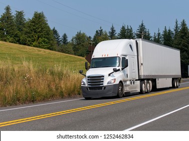 White Modern Bonnet Professional Technological Big Rig Semi Truck Transporting Dry Van Semi Trailer With Commercial Cargo On The Road With Trees And Summer Meadow Background