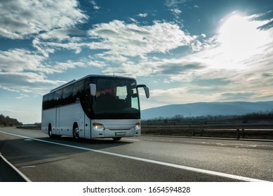 Белый Современный комфортабельный туристический автобус, проезжающий по шоссе на ярком солнечном закате. Концепция туристического и автобусного туризма. Поездка и путешествие на автомобиле