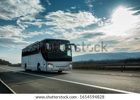 White Modern comfortable tourist bus driving through highway at bright sunny sunset. Travel and coach tourism concept. Trip and journey by vehicle