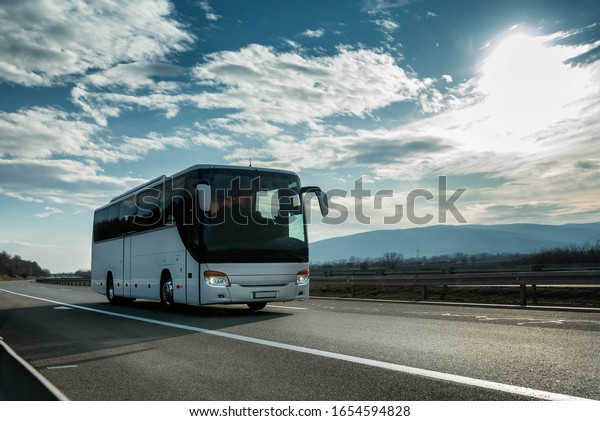 White Modern comfortable tourist bus driving\
through highway at bright sunny sunset. Travel and coach tourism\
concept. Trip and journey by\
vehicle