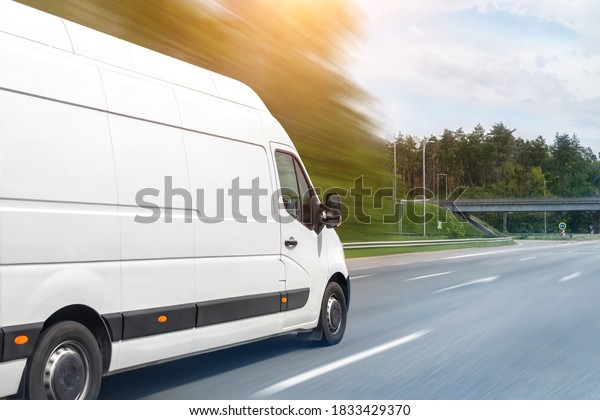 White modern delivery small shipment cargo courier\
van moving fast on motorway road to city urban suburb. Busines\
distribution and logistics express service. Mini bus driving on\
highway on sunny day