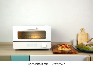 white modern design toaster oven is on the wooden table with pizza and homemade bread toast white cement wall background in minimal design kitchen