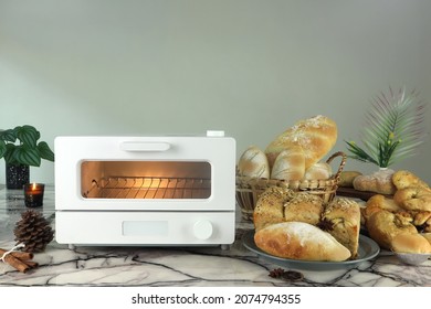white modern design toaster oven is on the table with homemade toast breads , pinecone, cinnamon sticks, anise star and plants on grey cement wall background in the kitchen room during chritmas party