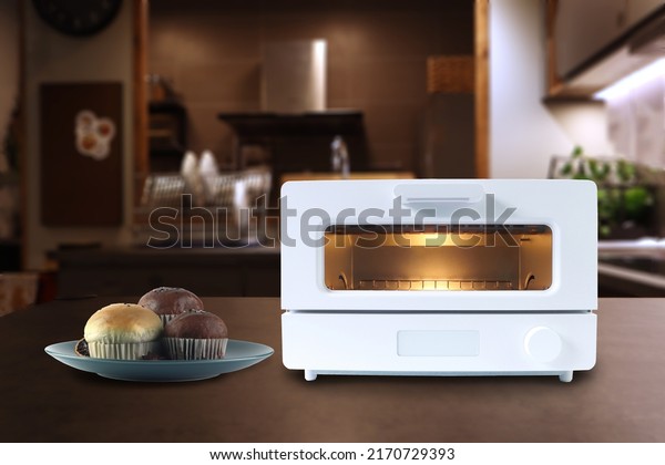 white modern design\
toaster oven is on the wooden table with homemade cup cake\
chocolate muffin on background of nice design kitchen for making\
breakfast in the morning