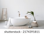 White modern tub in minimalistics bathroom interior. Porcelain bathtub with classic design in comfortable apartment or hotel room. Home decor and houseplant in spa centre