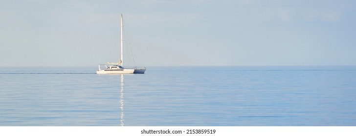 White Modern Yacht (catamaran) Sailing In An Open Caribbean Sea At Sunset. Clear Blue Sky, Symmetry Reflections In The Water. Idyllic Seascape. Travel Destinations, Sport, Leisure Activity, Recreation