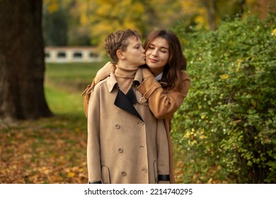 White Mom Hugs Teen Age Son, Child Kisses Her Cheek In Beautiful Park. Happy Motherhood, Childhood.Feeling Trust And Protection. Mothers Day,  International Child Protection Day. Horizontal Plane 