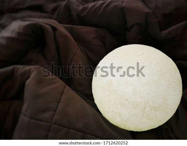 White moon\
lamp on dark color blanket in\
bedroom.
