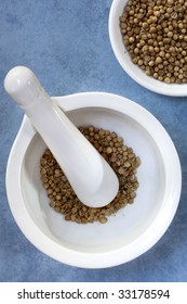 White Mortar And Pestle Grinding Coriander Or Cilantro Seeds.  Overhead View.