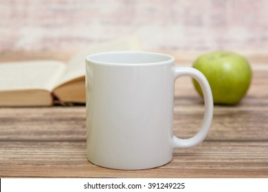 White mug with book and apple behind it