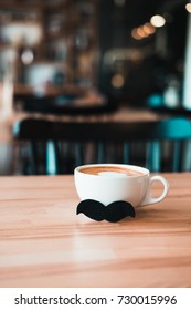 White Mug Of Coffee With Moustache On Wooden Table At Coffee Shop