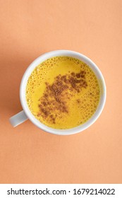 White mug of golden milk with turmeric and cinnamon powder on a light marinade background. A healthy drink to enhance immunity.
