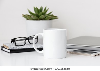 White mug mockup, modern workspace with laptop, notebooks, eyeglasses and succulent plant