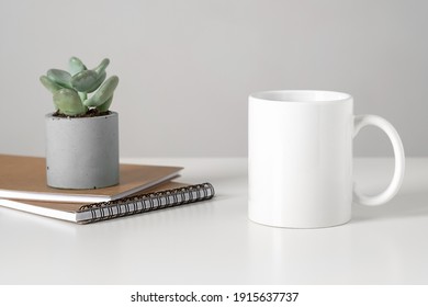 White Mug Mockup On Table In Minimalist Interior, Business Concept, Succulent And Notepads. Template, Layout For Your Design, Advertising, Logo With Copy Space. Cup On Light Gray Background.