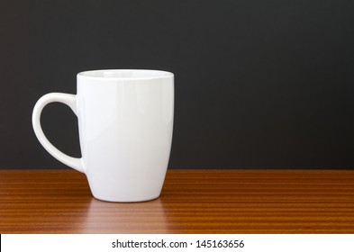 White Mug On Dark Wooden Table With Black Wall