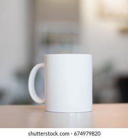 White mug on table and modern room background. Blank drink cup for your design. Can put text, image, and logo.