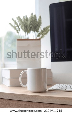 White mug on the working desk near window. Blank drink mug or cup for your design. Can put text, image, and logo.