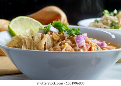 White Navy Bean Chicken Chili With Tortilla Strips Lime Cilantro And Shredded Cheese Garnish