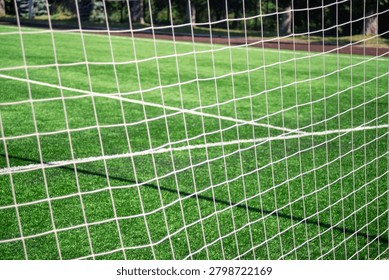 White net frames green grass field. Shadows stretch across turf from sunlit sky. Grid pattern invites sport, game, or training. Perfect for fitness, recreation, or outdoor sports